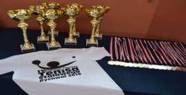 IV Gminny Turniej Tenisa Stołowego_2 zdjęcie przedstawia: puchary, medale i białą koszulke z napisem