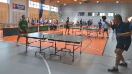 IV Gminny Turniej Tenisa Stołowego_8 zdjecie przedstawia: mężczyzn grających w tenisa stołowego na sali gimnastycznej i w  tle inne osoby grające