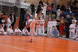 Mistrzostwa Oyama Karate w Kata_2 zdjęcie przedstawia: dziewczynkę podnoszącą nogę, w tle ludzi obserwujących