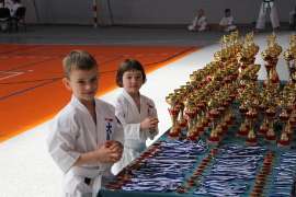 Mistrzostwa Oyama Karate w Kata_5 zdjęcie przedstawia: dziewczynkę i chłopca stojących przy stole z pucharami i medalami