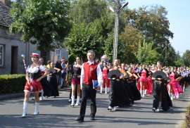Przedszkolaki_1: Zdjęcie przedstawia grupę osób maszerujących przez ulicę. Ubrani są w biało-czerwono-czarne stroje. 