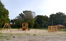 Place zabaw_4: Zdjęcie przedstawia drewniane huśtawki, drabinki i domki stojące na piasku
