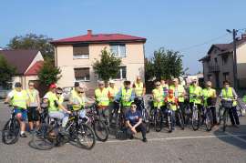 UTW Rychwał: zdjęcie przedstawia grupę śpiewających ludzi w kamizelkach odblaskowych z rowerami